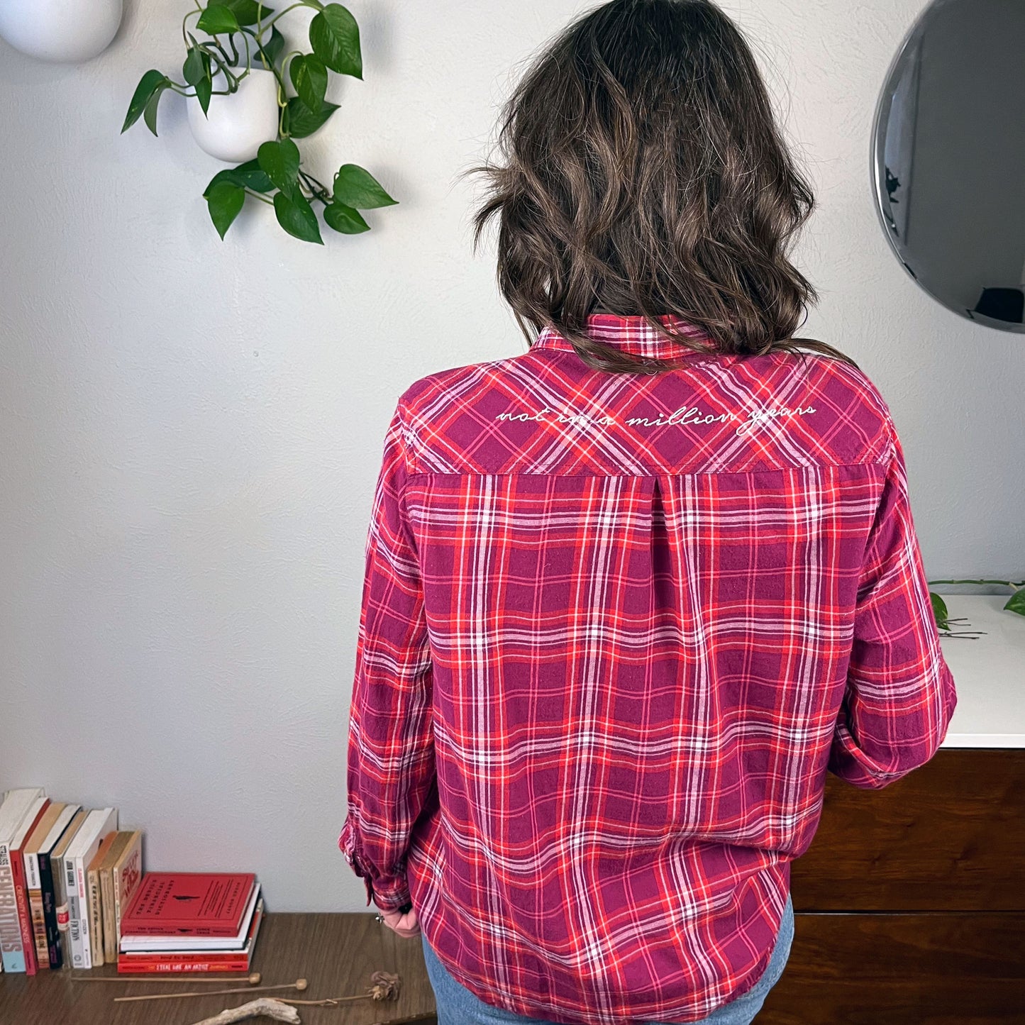 back view of a woman wearing a berry colored plaid flannel shirt with scripty words not in a million years hand embroidered on the back yoke