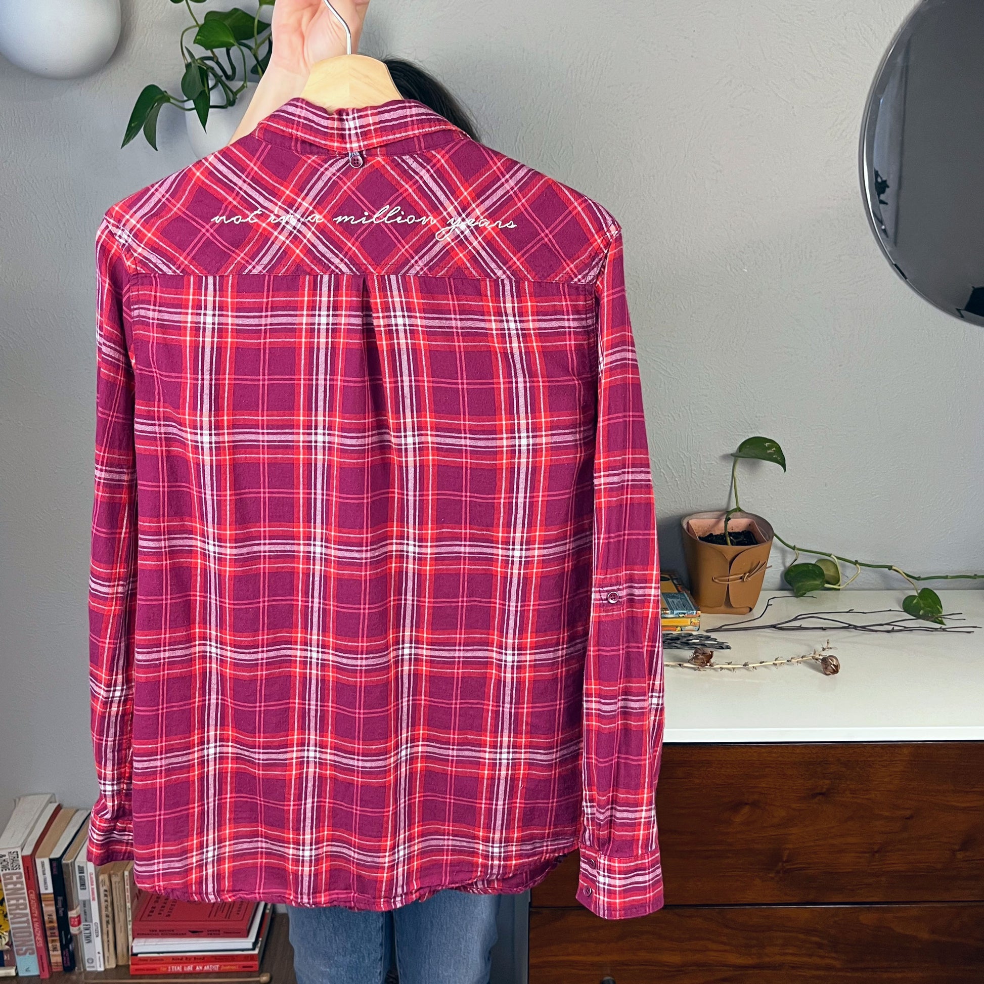 back view of a berry colored plaid flannel shirt on a hanger with scripty words not in a million years hand embroidered on the back yoke