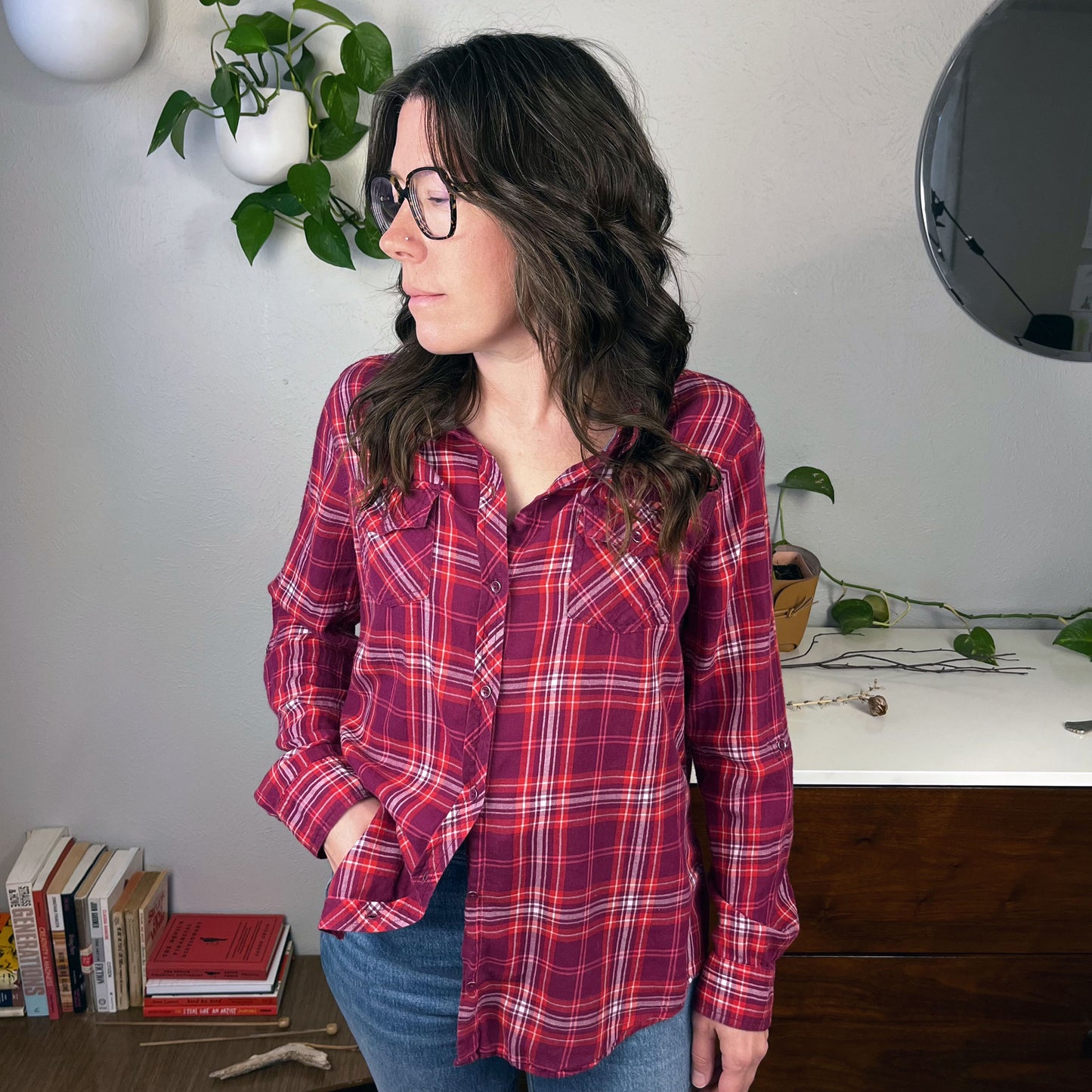 a woman with glasses wearing a berry plaid flannel shirt standing in front of a few pothos plants