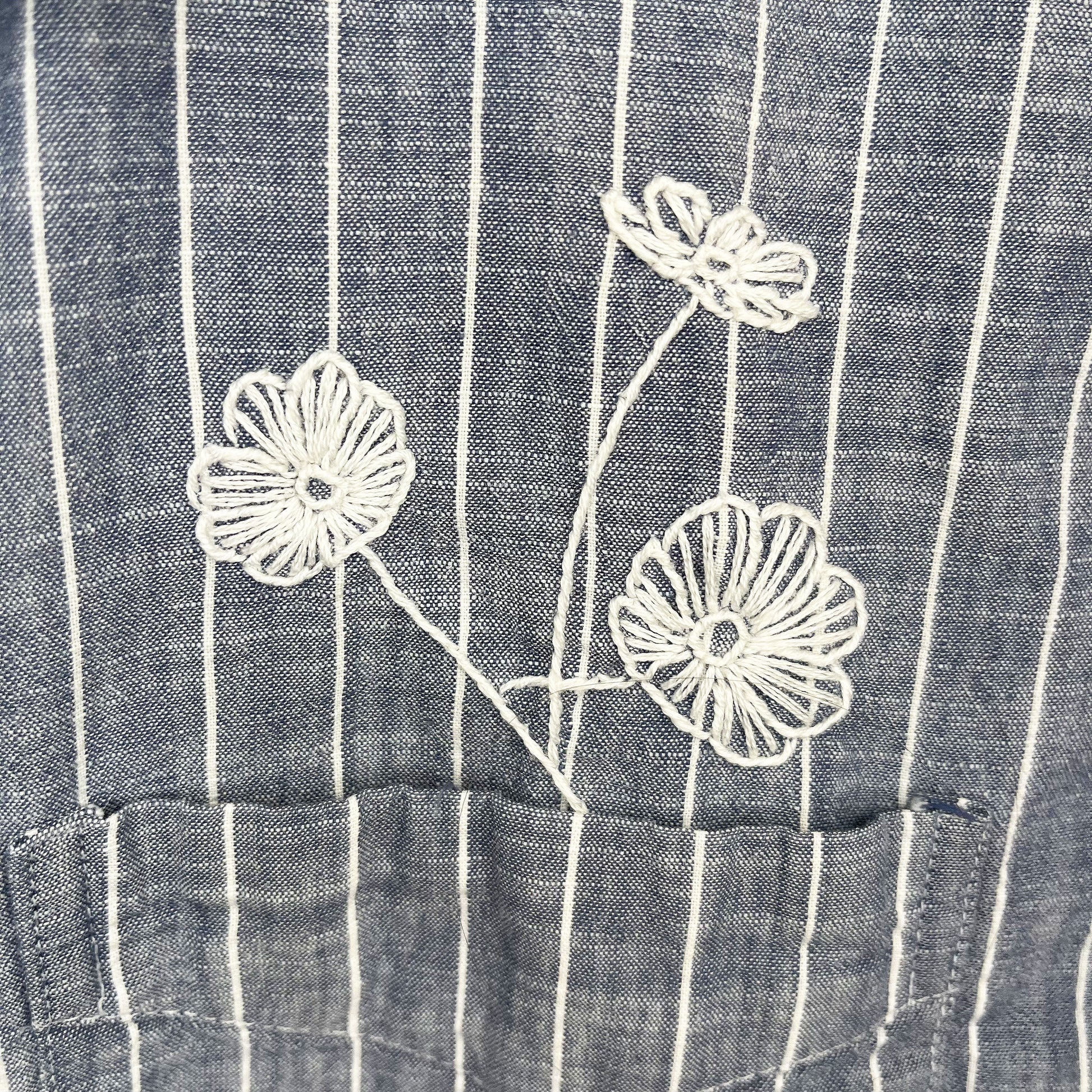 close up view of a striped chambray shirt with white hand embroidered poppies coming out of the chest pocket 