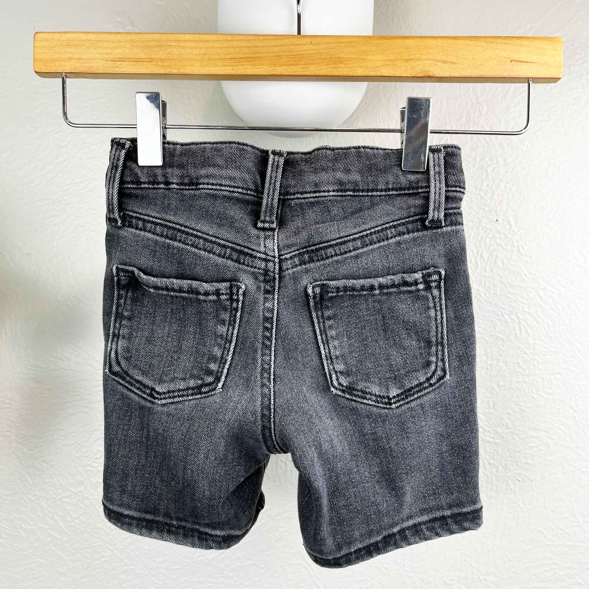 back view of black jean shorts hanging from a wood hanger