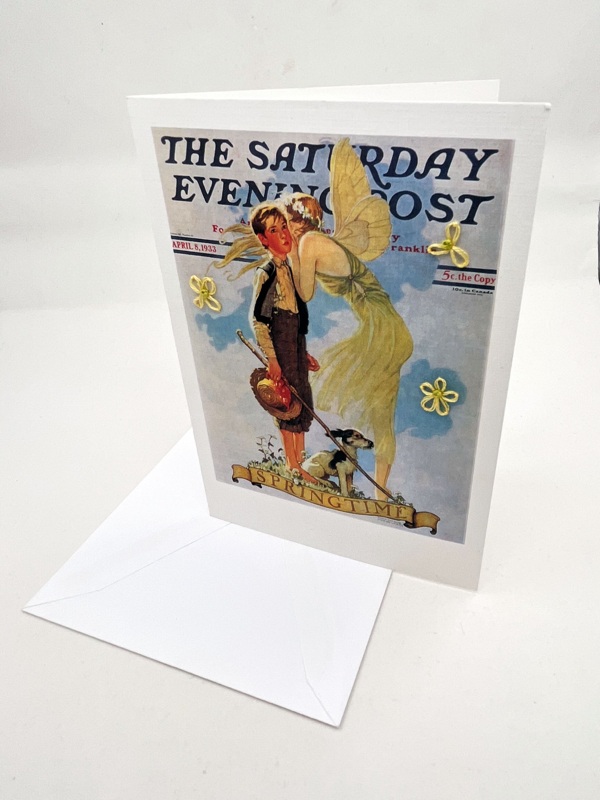 greeting card with a print of an issue of The Saturday Evening Post, a picture of a fairy whispering in a boys ear, a with hand embroidered flowers around them