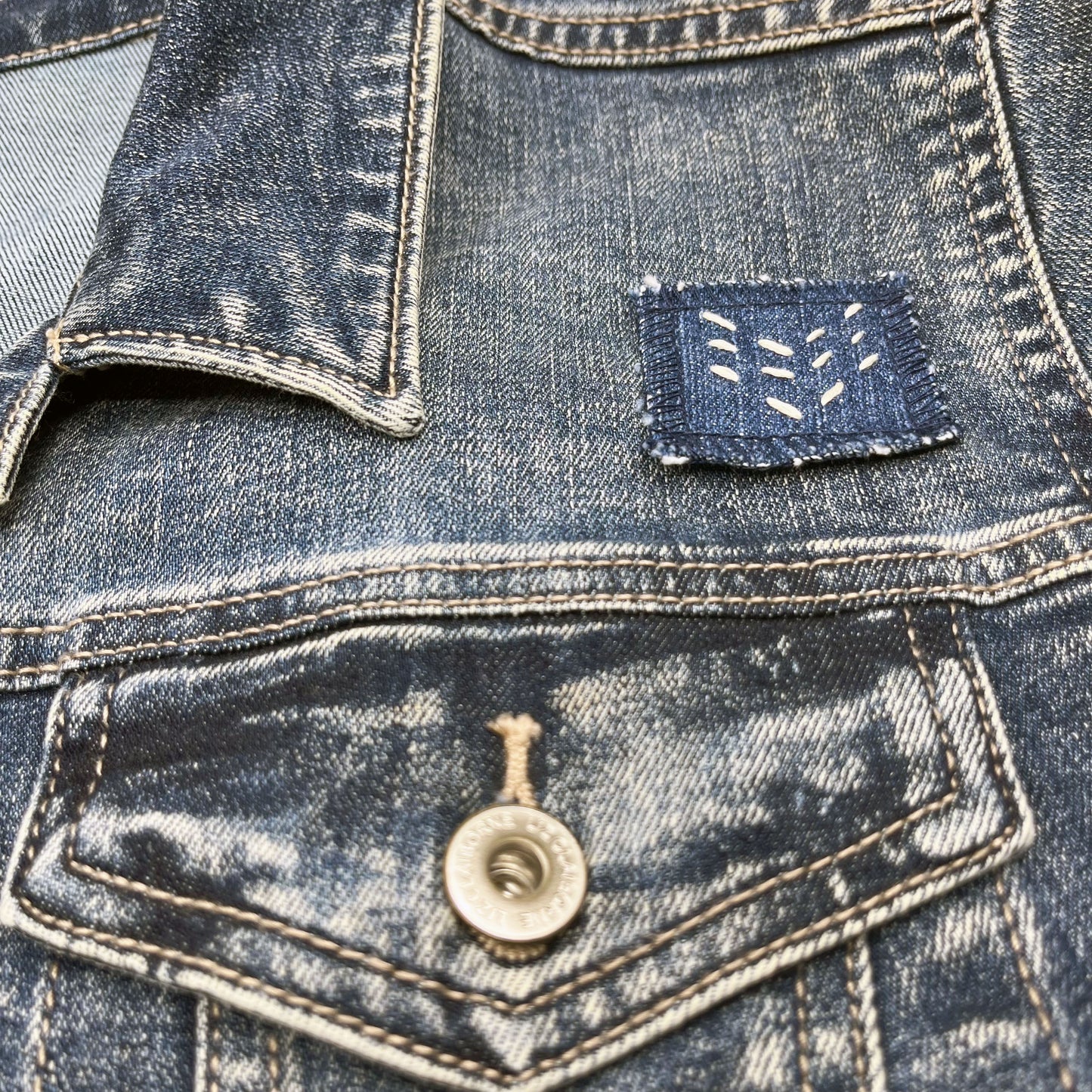 square denim patch with running stitches in ecru of three chevron lines on a denim jacket