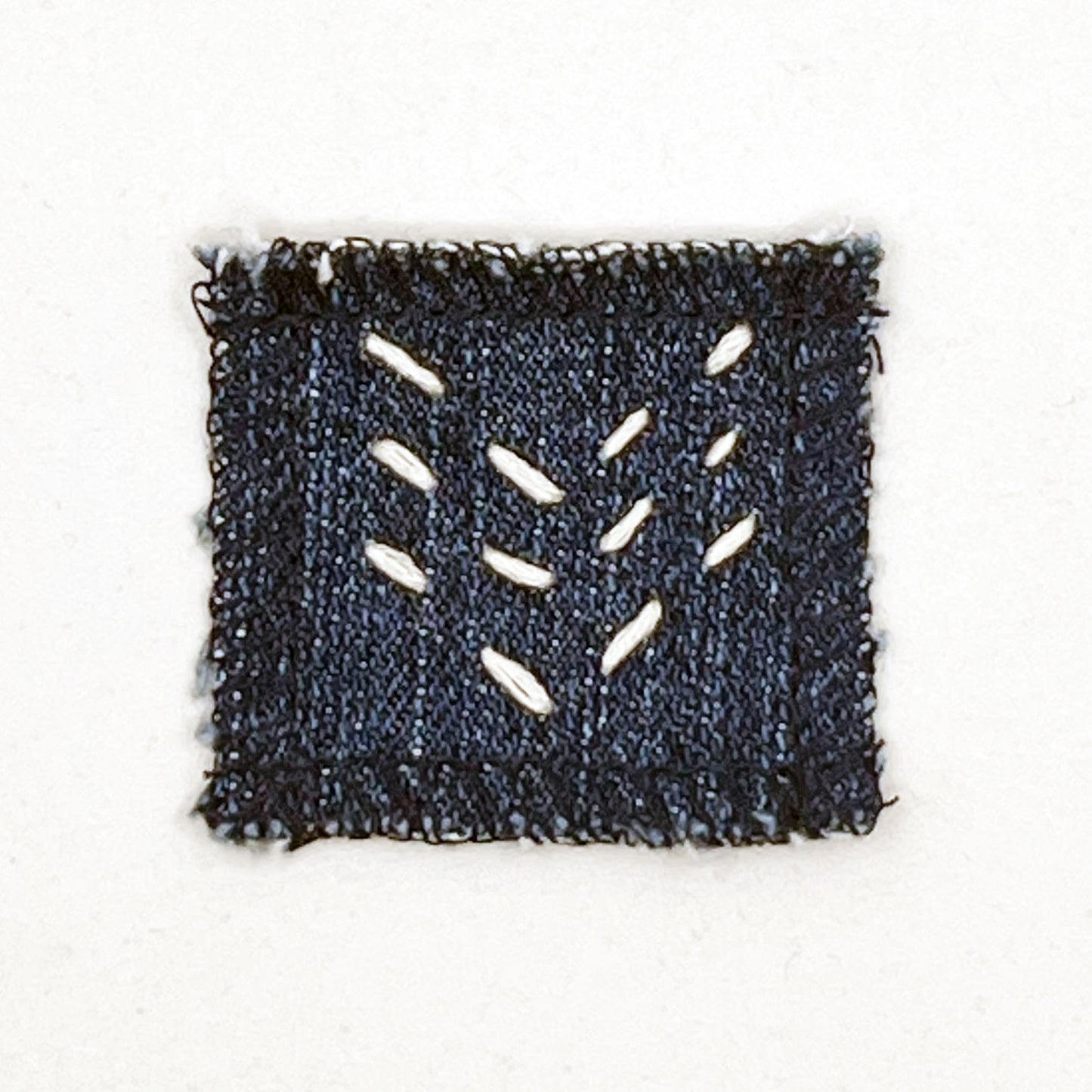 square denim patch with running stitches in ecru of three chevron lines on a white background