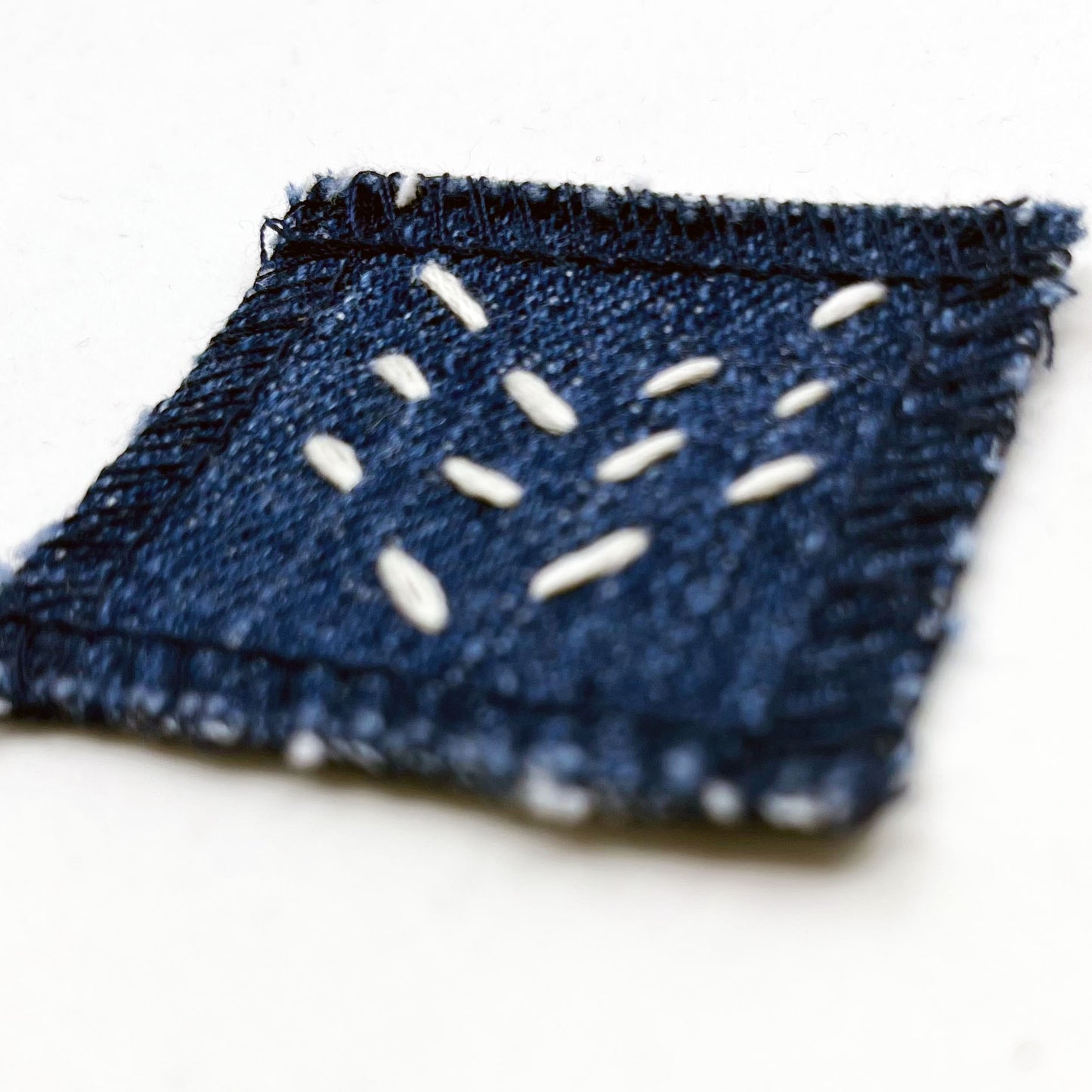 square denim patch with running stitches in ecru of three chevron lines on a white background