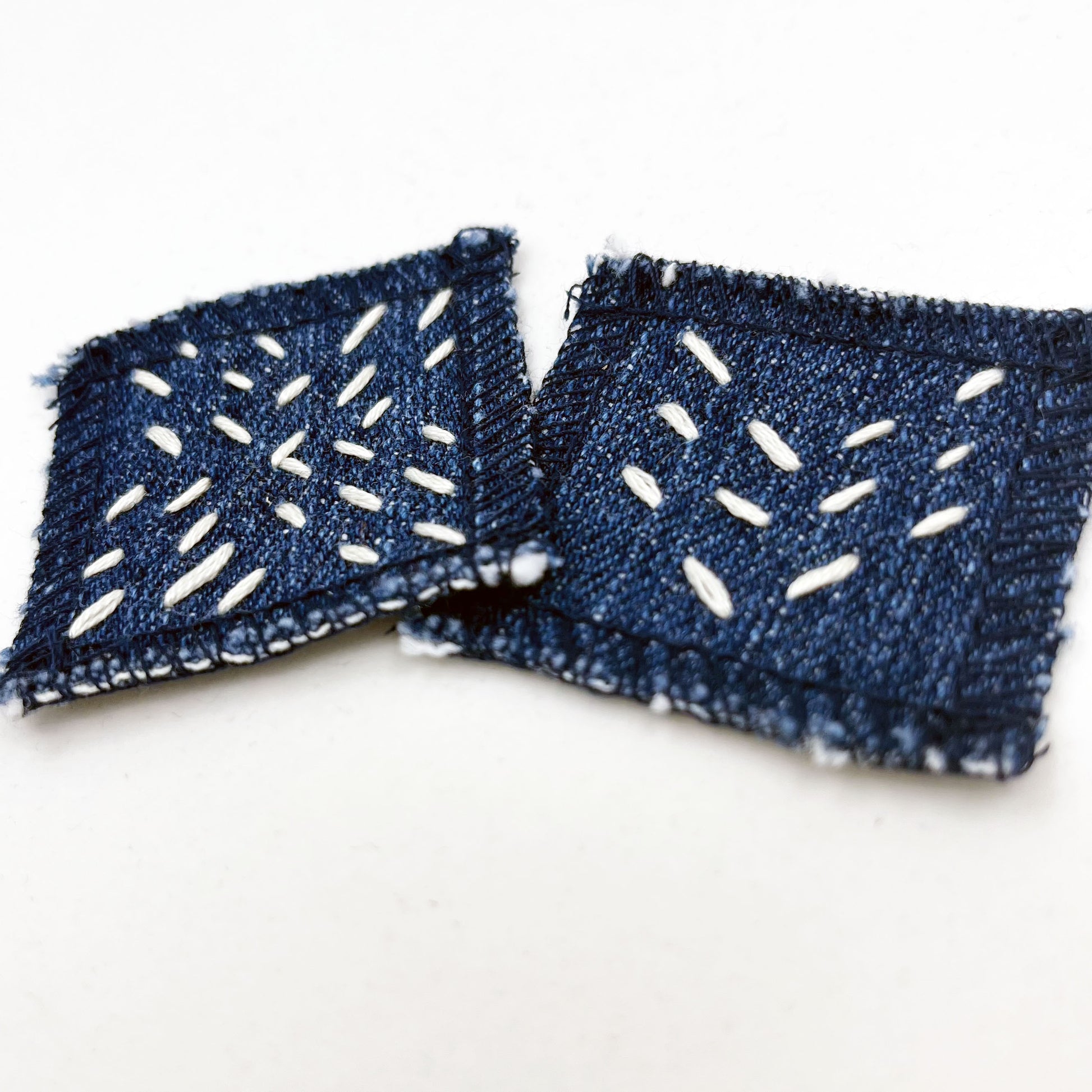 two square denim patches with running stitches in ecru of three chevron lines and a repeating x pattern on a white background