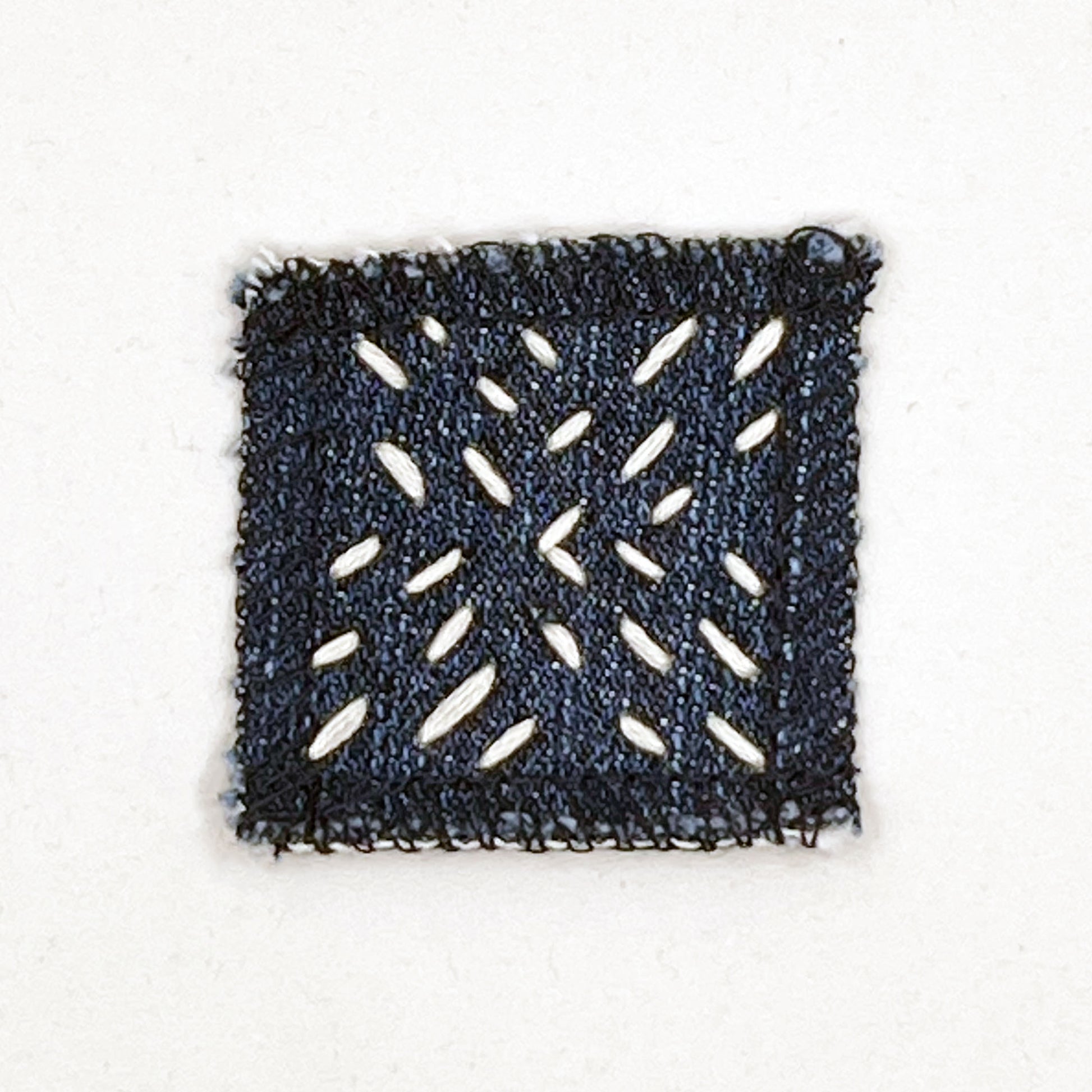 square denim patch with running stitches in a repeating x pattern on a white background