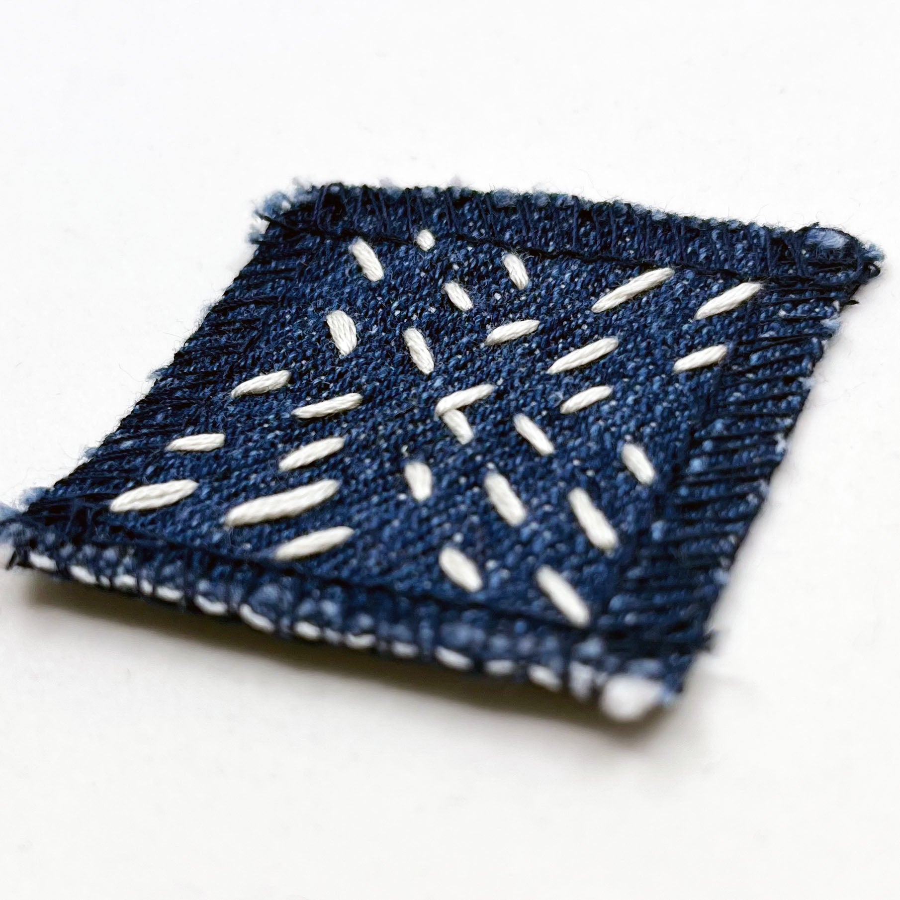 square denim patch with running stitches in a repeating x pattern on a white background