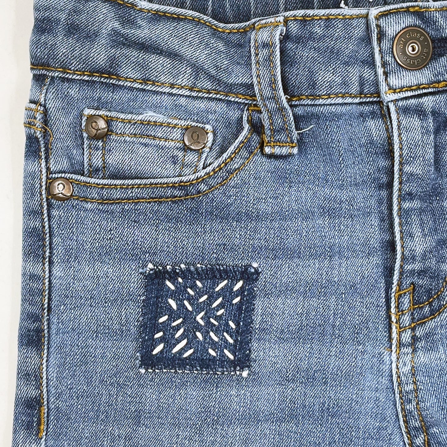 square denim patch with running stitches in a repeating x pattern on a pair of kids jeans