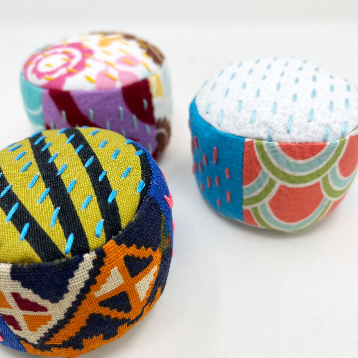 a group of 3 colorful pincushions on a white counter, with sashiko stitching in contrasting colors