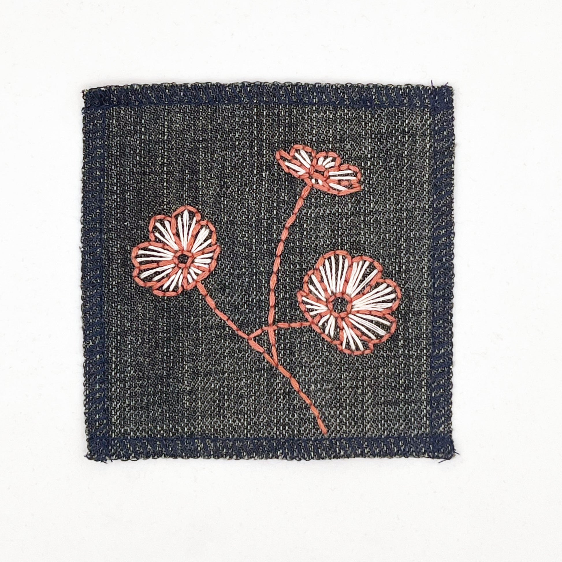 a square denim patch with three poppies hand embroidered on it, the outline of the petals and stem in clay colored thread and the fill lines in peach