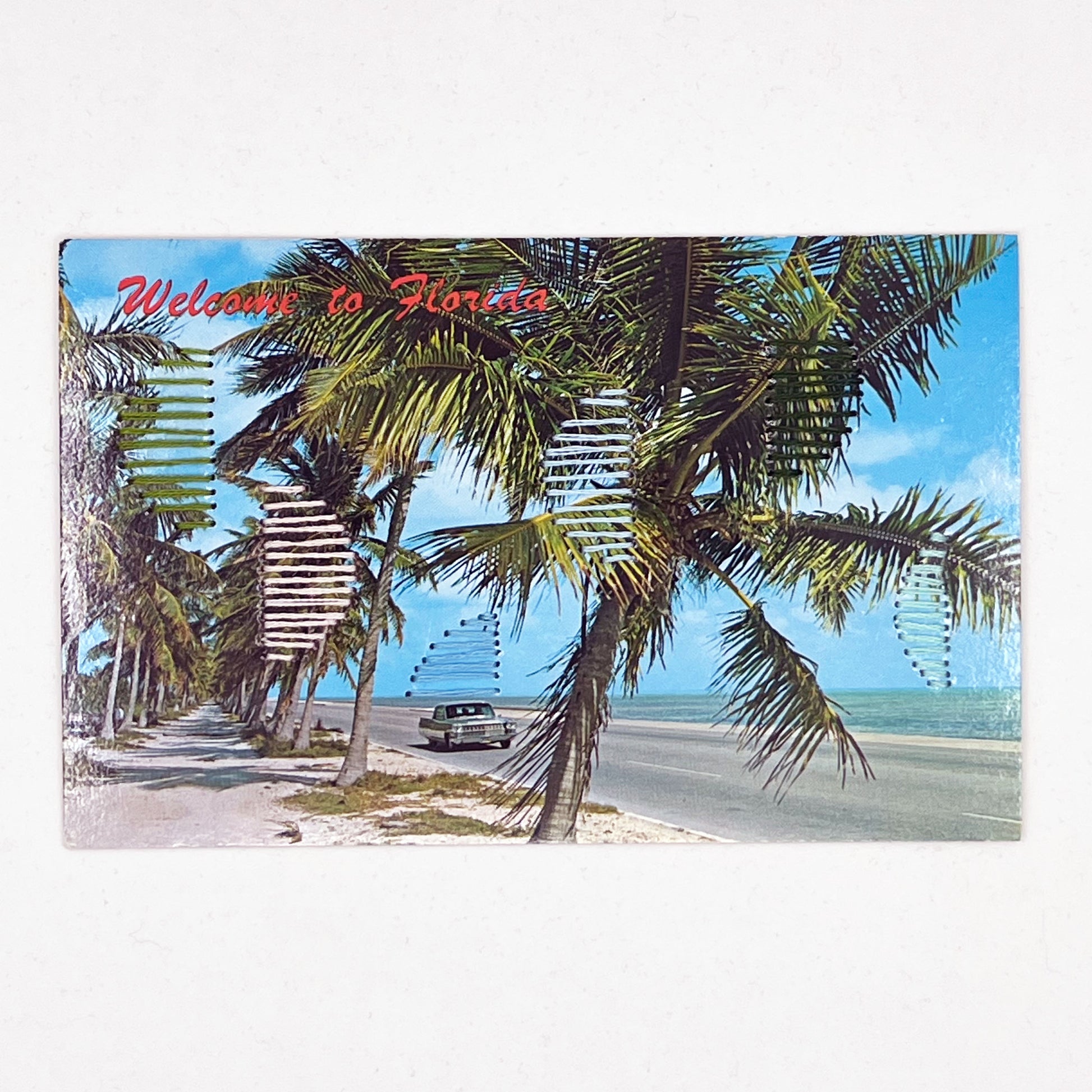 an old postcard of a Florida beach, with hand embroidered half circles randomly placed in greens blues and peaches, on a white surface