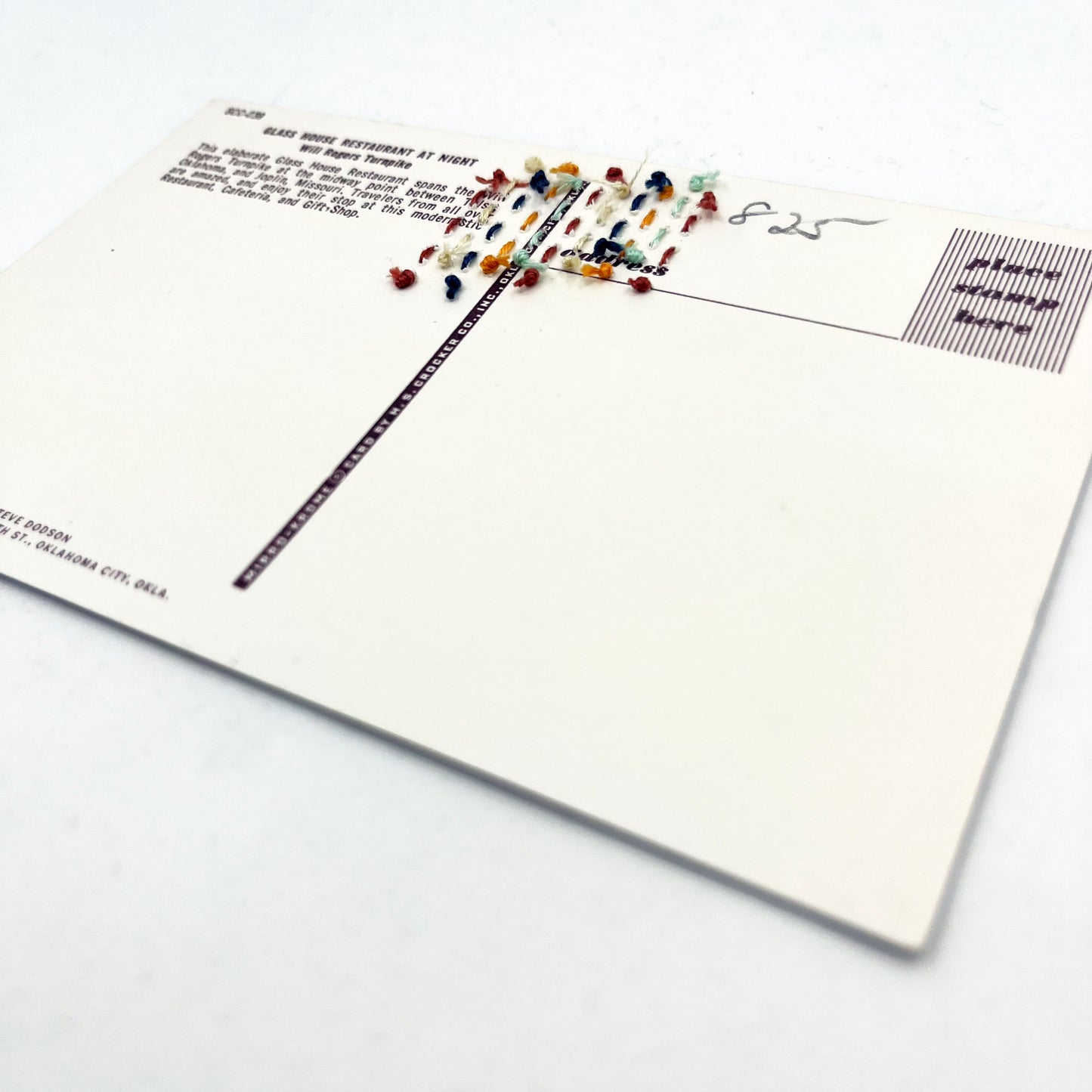 back side of an old postcard of the Glass House rest stop restaurant, with multicolored hand embroidered lines, on a white surface