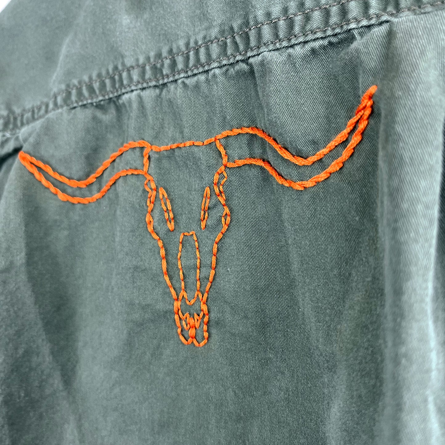 close up view of an outline of a longhorn skull embroidered in orange on the back of a green button up shirt