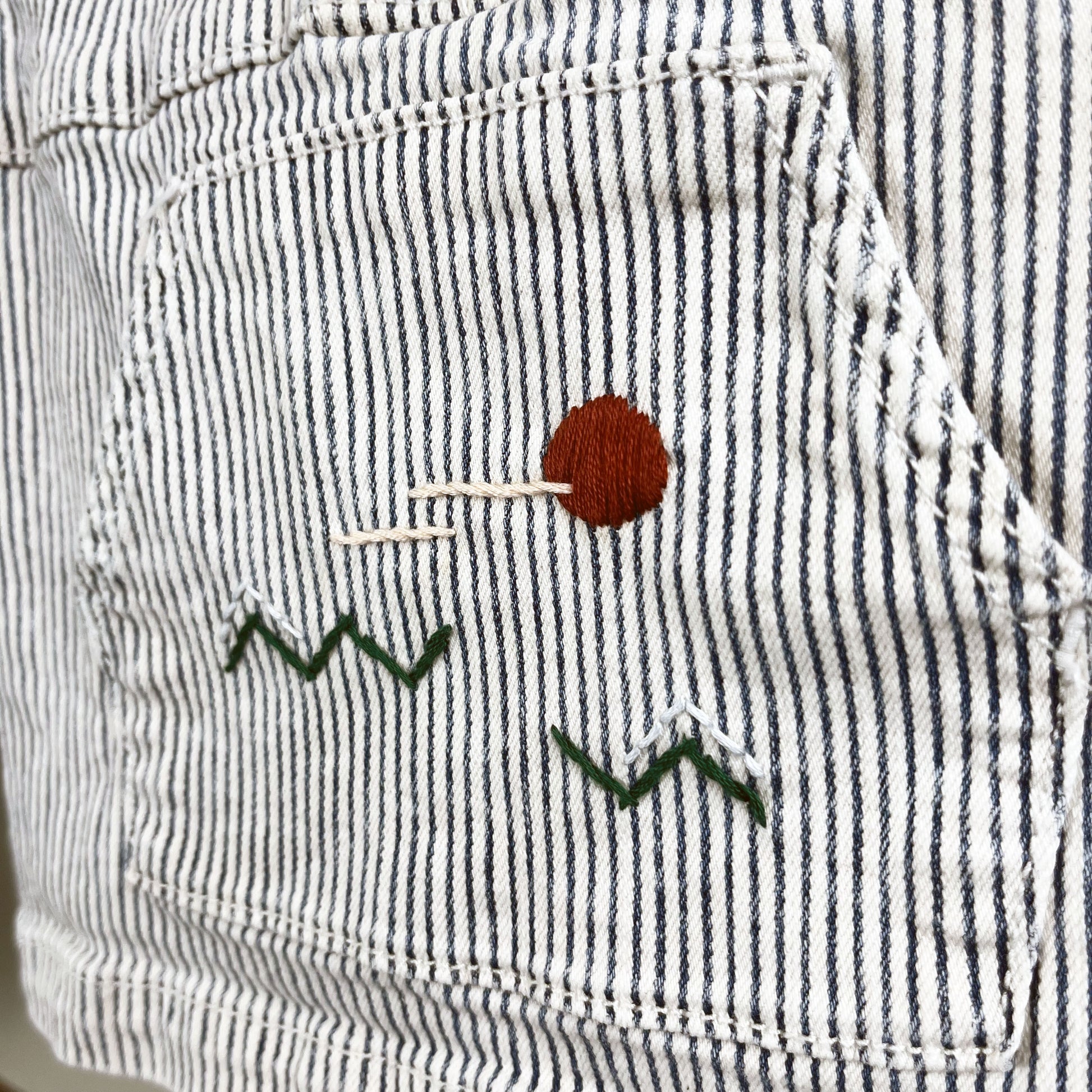 close up view of a railroad striped kangaroo pocket with a hand embroidered abstract landscape