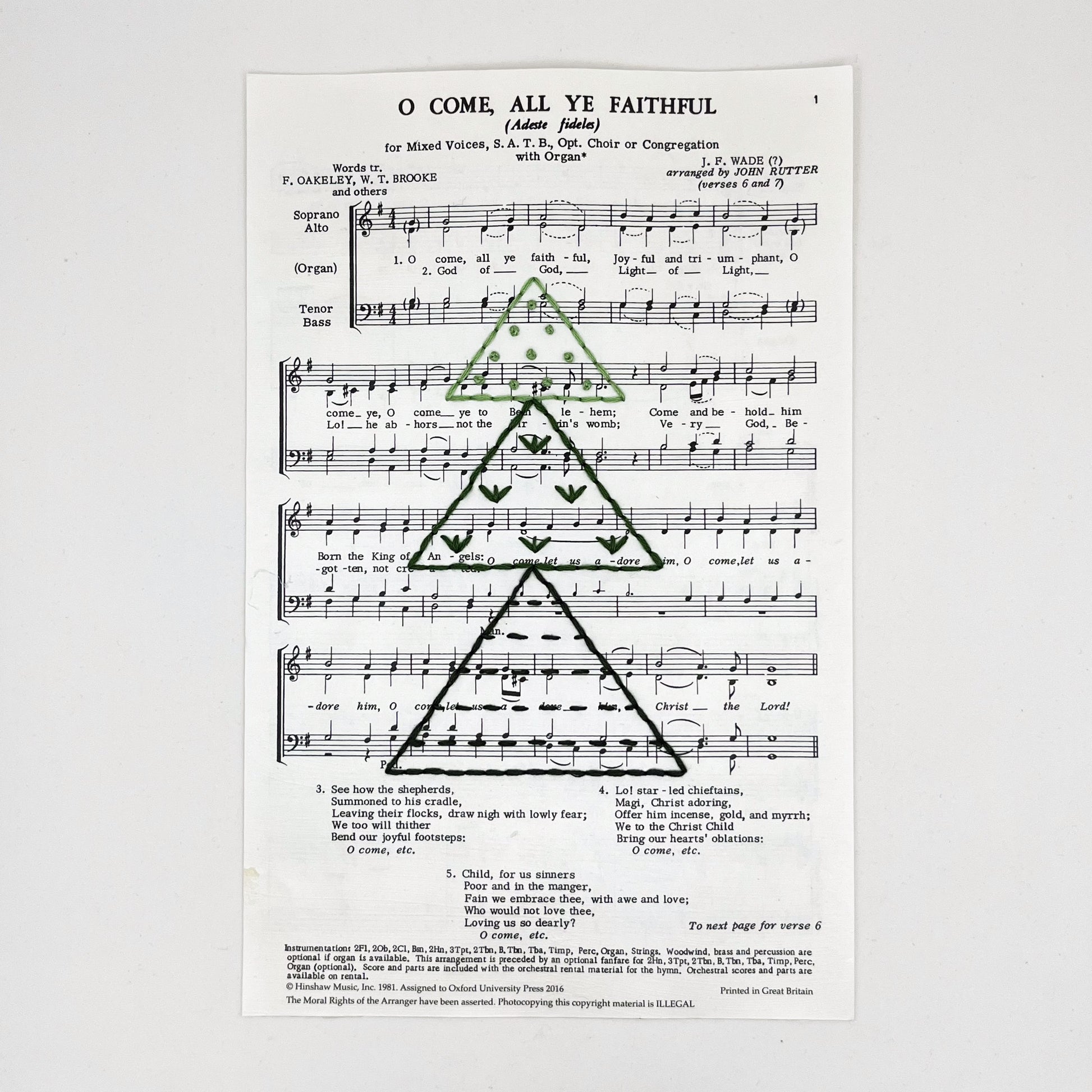 Christmas sheet music for the song O Come All Ye Faithful, hand stitched on with a Christmas tree made from triangles filled with different types of stitches, in shades of green thread