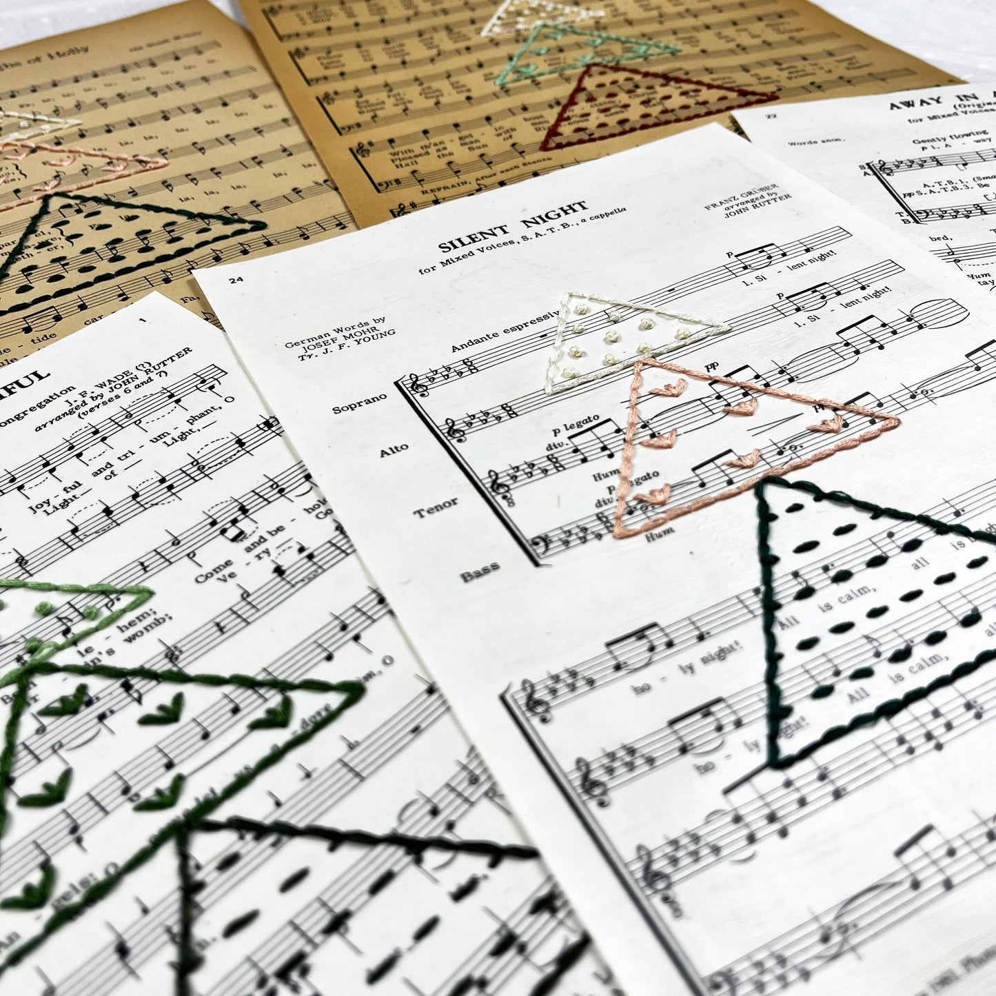 a group of Christmas sheet music, hand stitched on with a Christmas tree made from triangles filled with different types of stitches, in a variety of colors