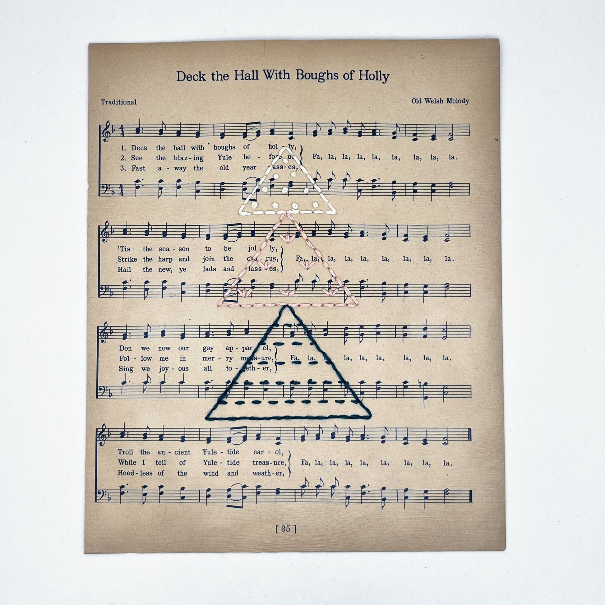 Christmas sheet music for the song Deck the Hall, hand stitched on with a Christmas tree made from triangles filled with different types of stitches, in green, peach and ivory thread, on a white background