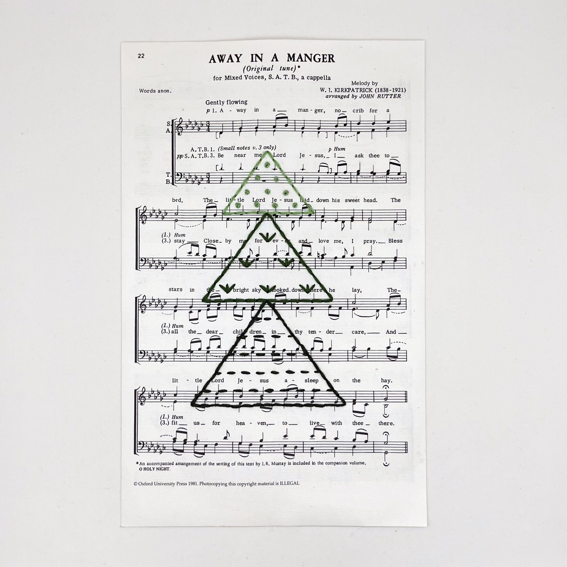 Christmas sheet music for the song Away in a Manger, hand stitched on with a Christmas tree made from triangles filled with different types of stitches, in shades of green thread