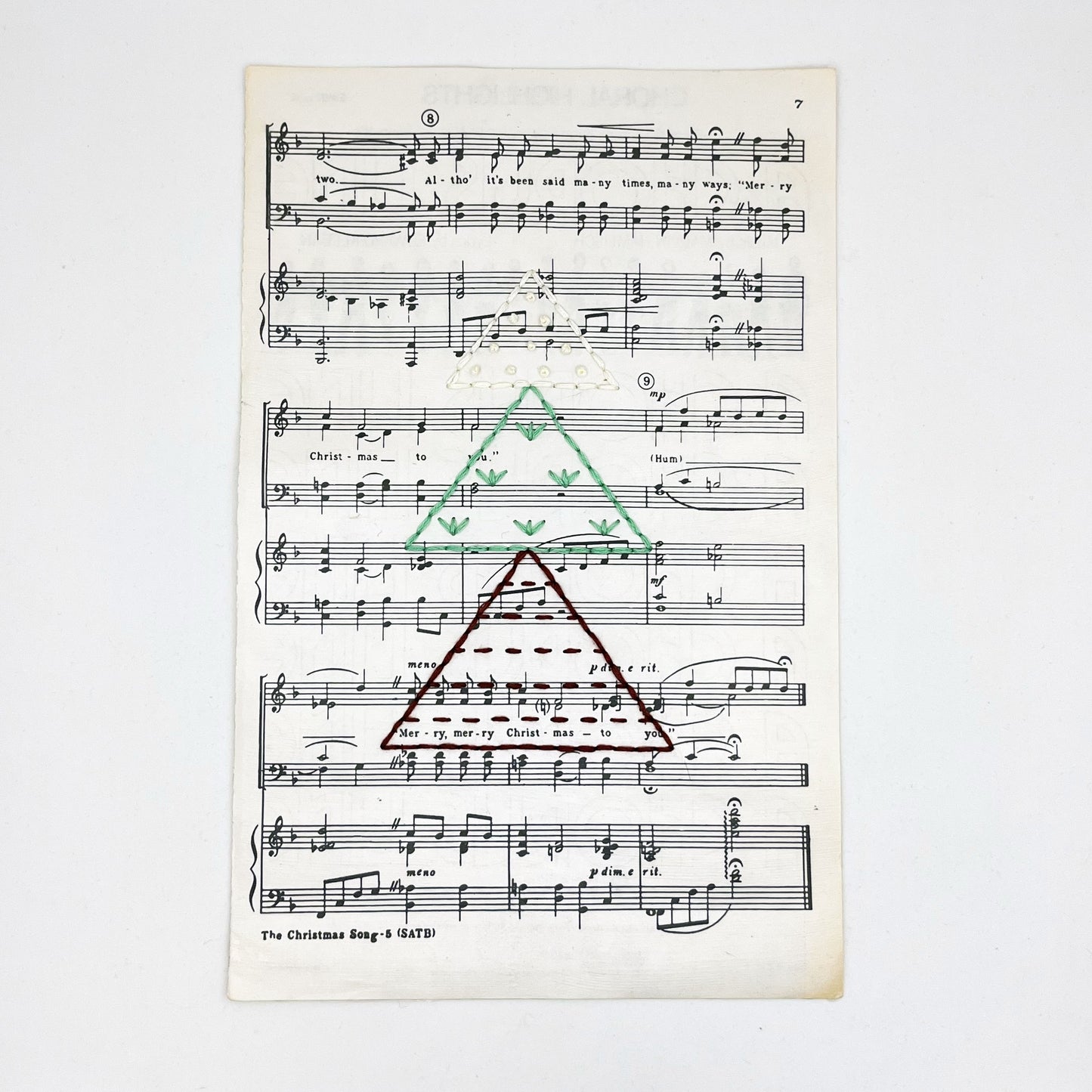 Christmas sheet music for the song The Christmas Song, hand stitched on with a Christmas tree made from triangles filled with different types of stitches, in red, green and ivory thread